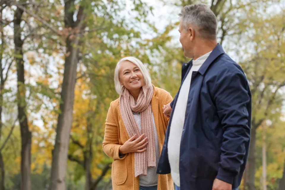 An older couple walking together on a tree-lined park path